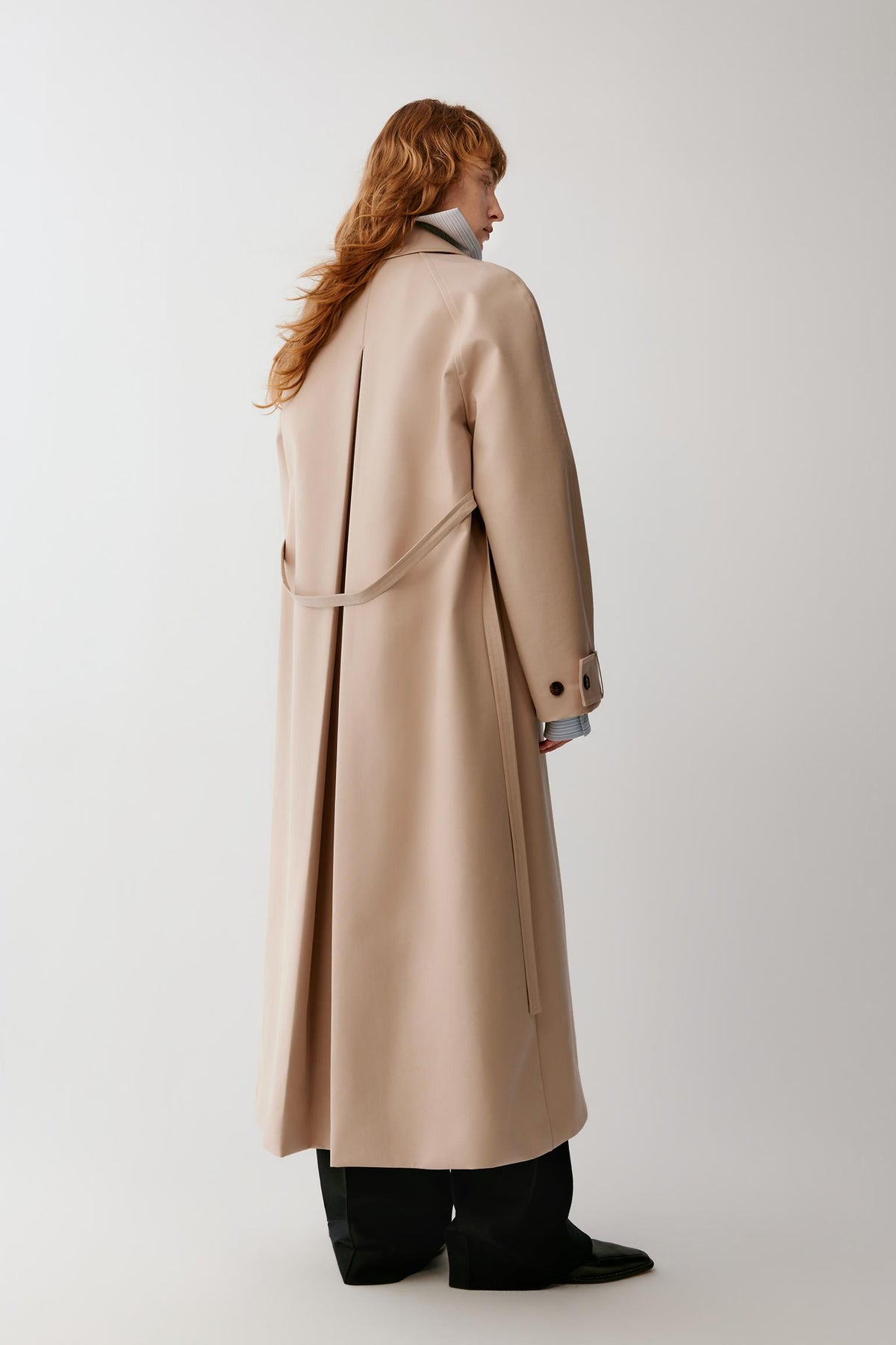 Back view highlighting the raglan sleeves, long silhouette and clean construction of the trench coat.