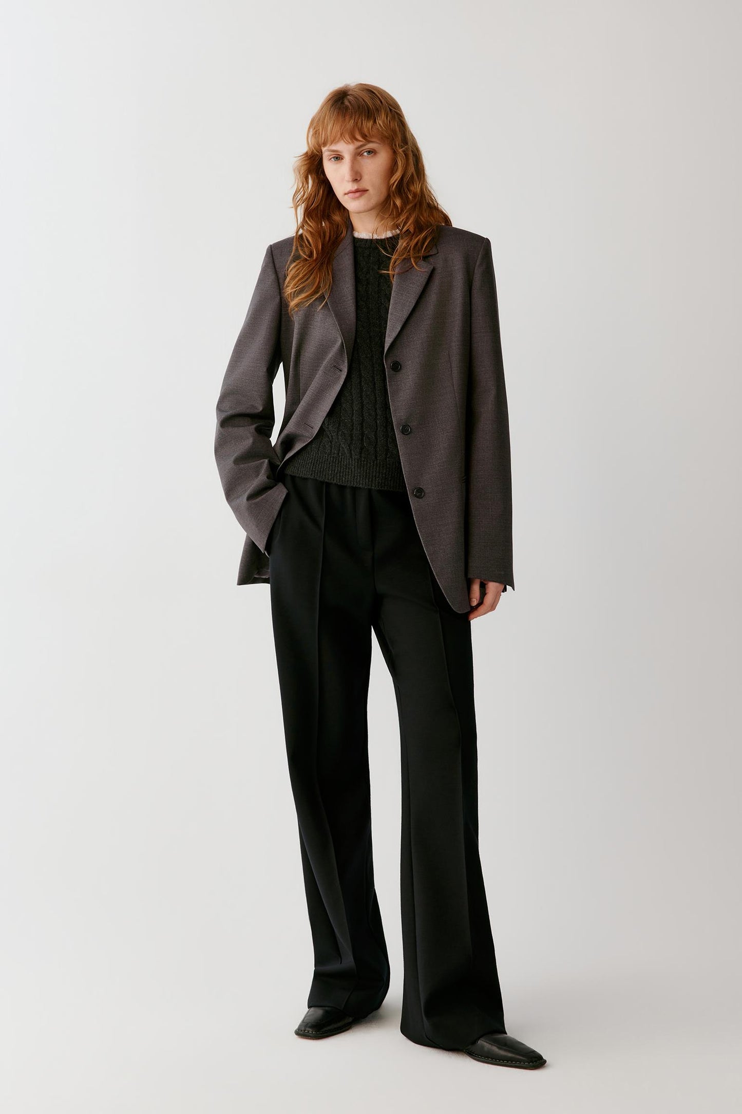 Full-length front view showing the grey melange wool blazer with black trousers, highlighting the straight cut and clean lines.