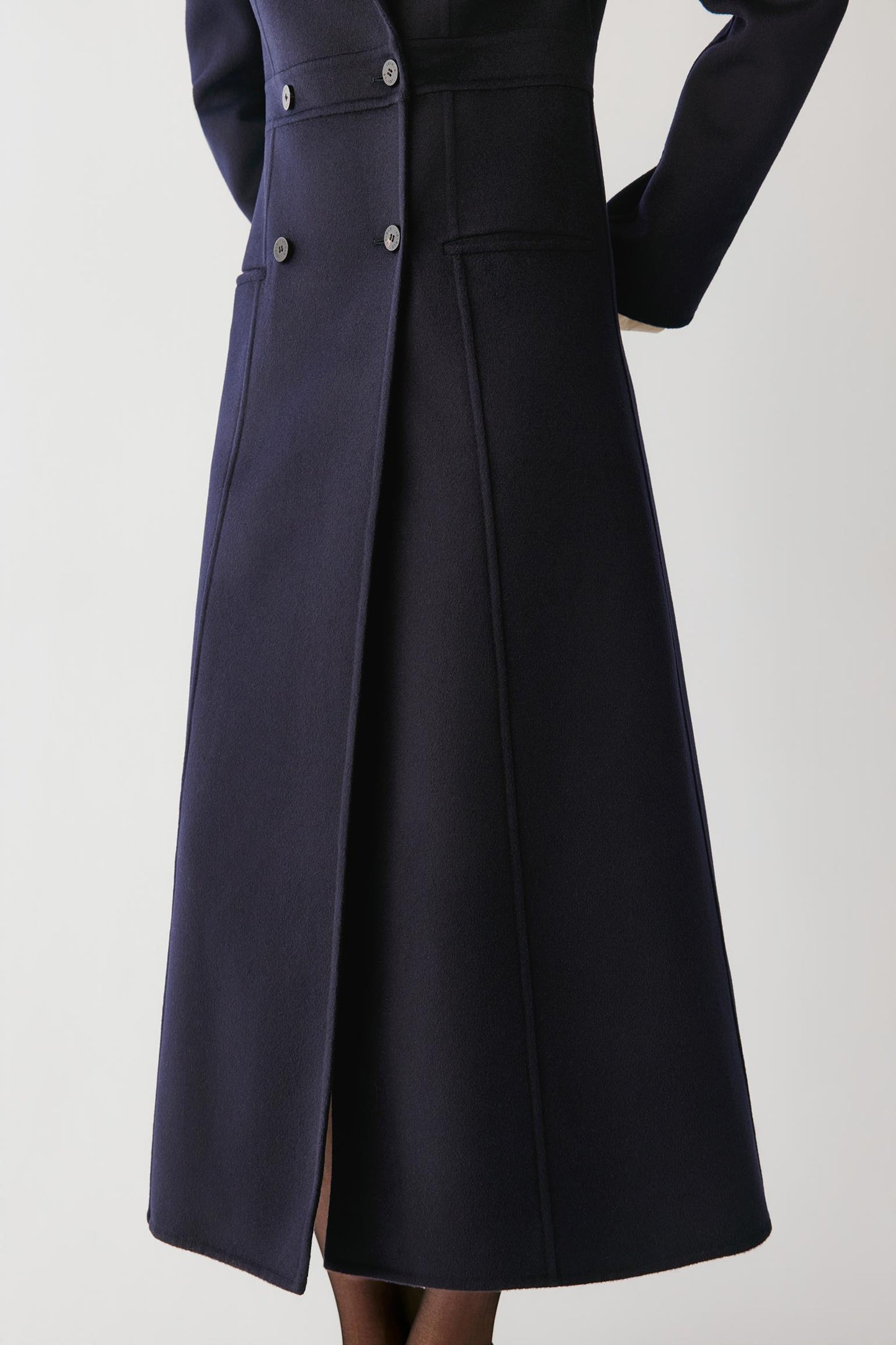 A dark navy blue wool-blend coat with a structured waist, double-breasted front, and front slit, shown on a model against a light gray background.