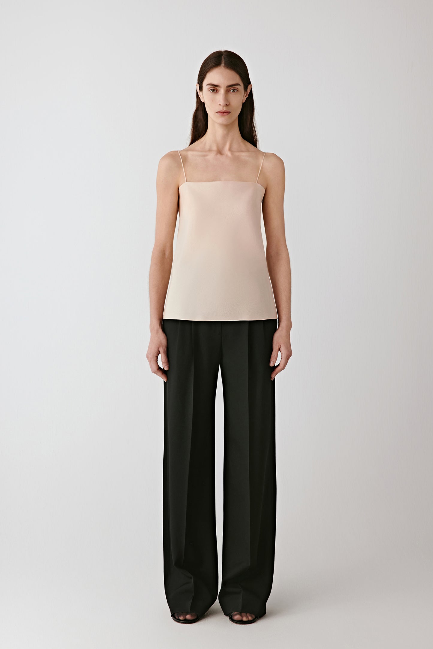 Full-length front view of the model wearing the deep black worsted wool gabardine trousers with a light beige top.