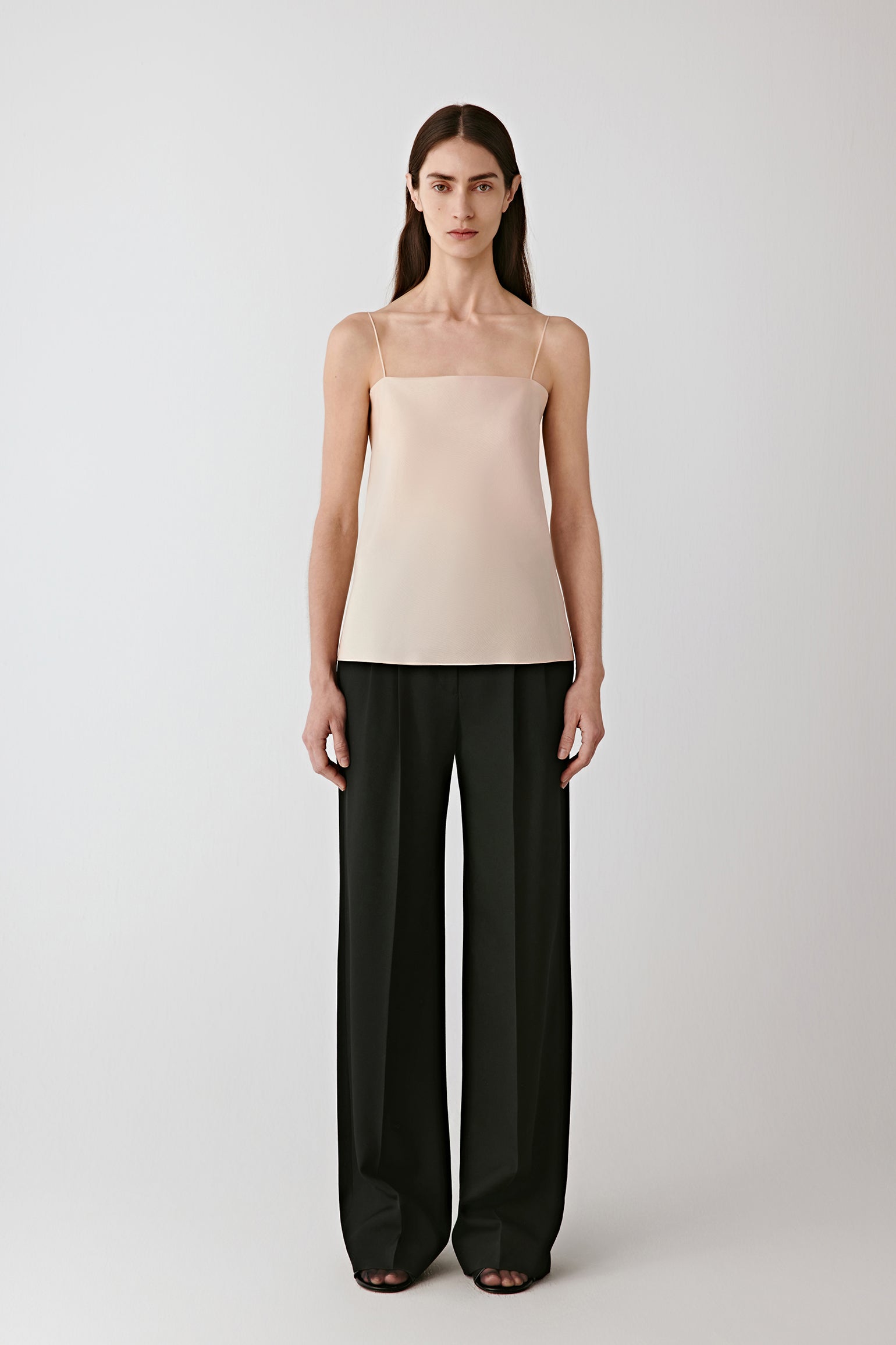 Full-length front view of the model wearing the deep black worsted wool gabardine trousers with a light beige top.