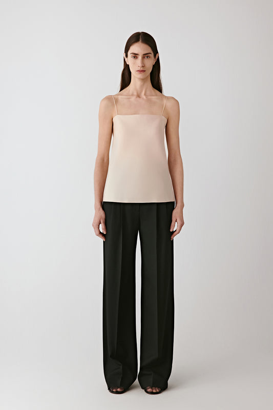 Full-length front view of the model wearing the deep black worsted wool gabardine trousers with a light beige top.