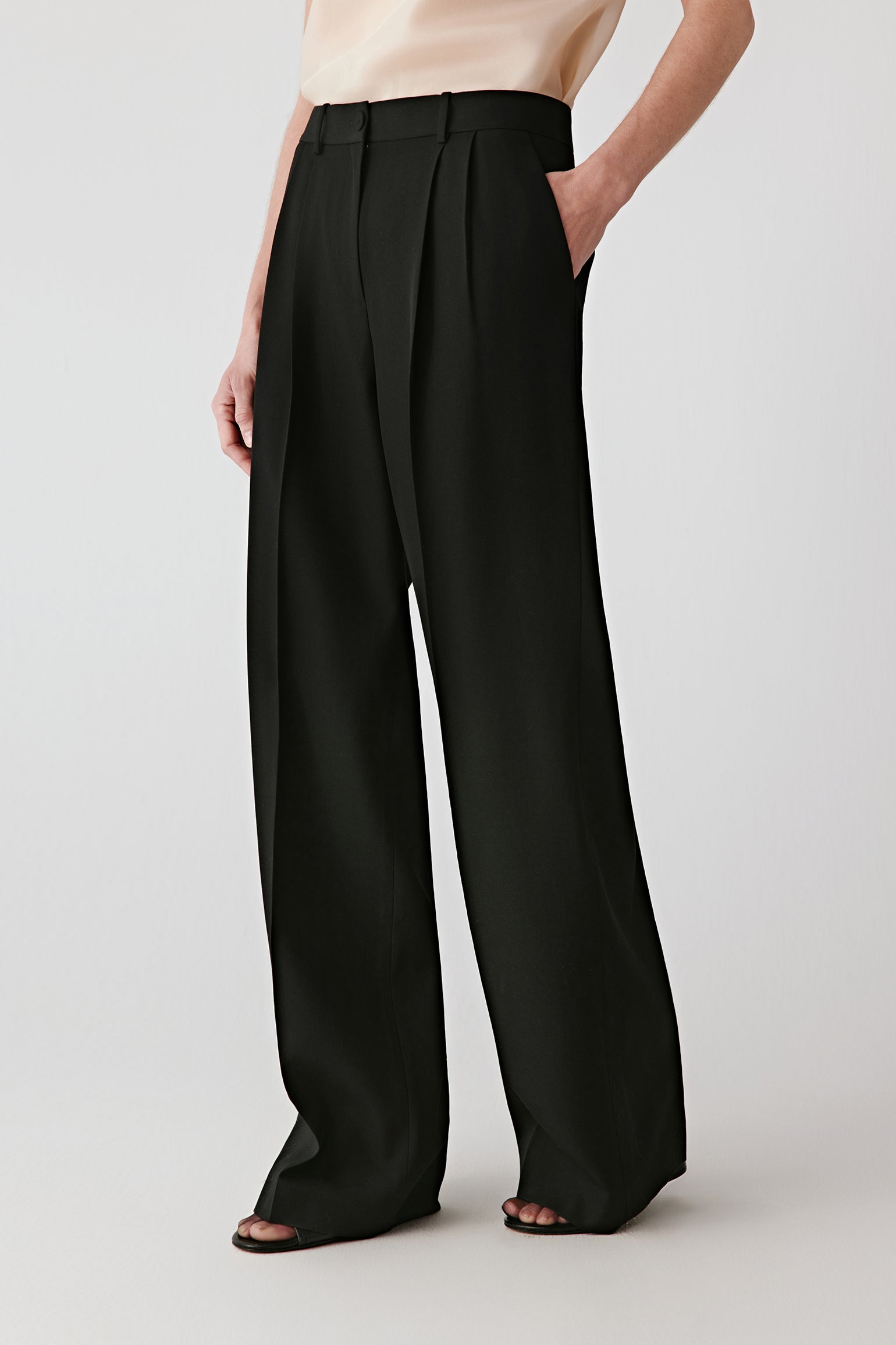 Three-quarter front view showing the high waist, sharp front pleats, and smooth drape of the fabric.