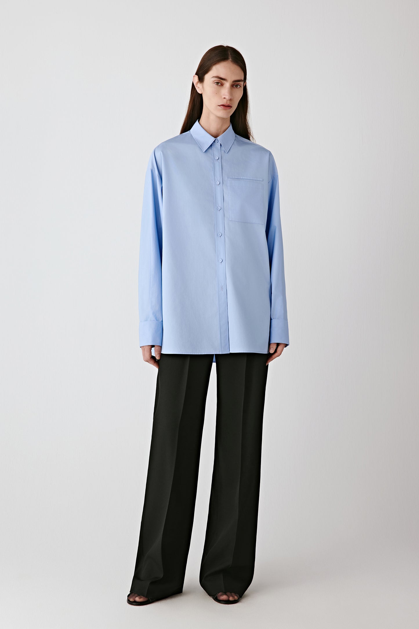 Full-length front view of the model wearing the light blue cotton satin shirt with black trousers.