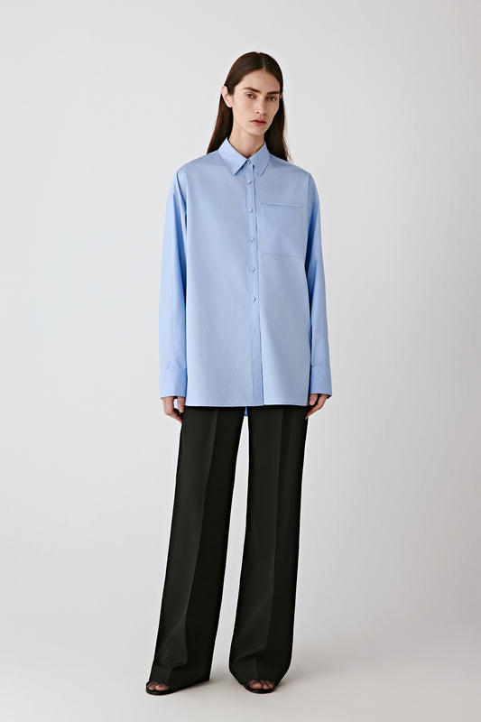 Full-length front view of the model wearing the light blue cotton satin shirt with black trousers.