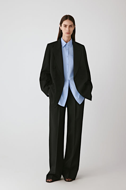 Front view of the black wool gabardine double-breasted jacket, worn over a light blue shirt, showing its tailored fit.