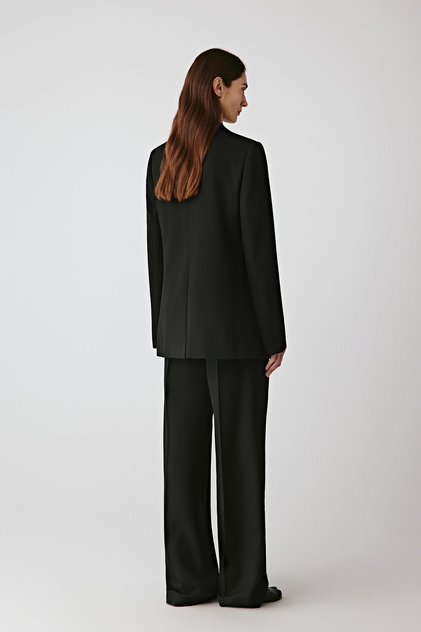 Back view of the black jacket, showing the fluid movement and precise tailoring.
