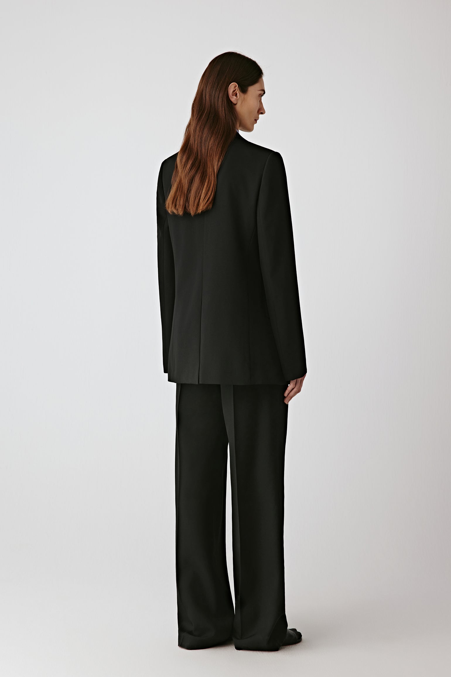 Back view of the black jacket, showing the fluid movement and precise tailoring.