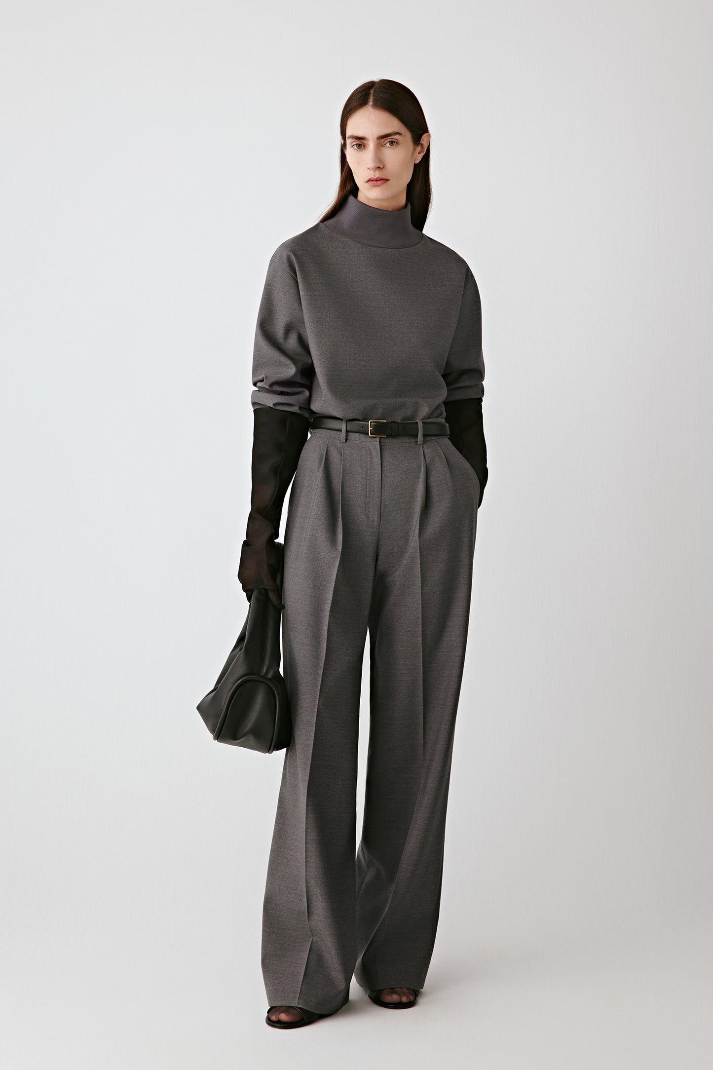 Full-length front view of the model wearing the grey melange satin-finish trousers.