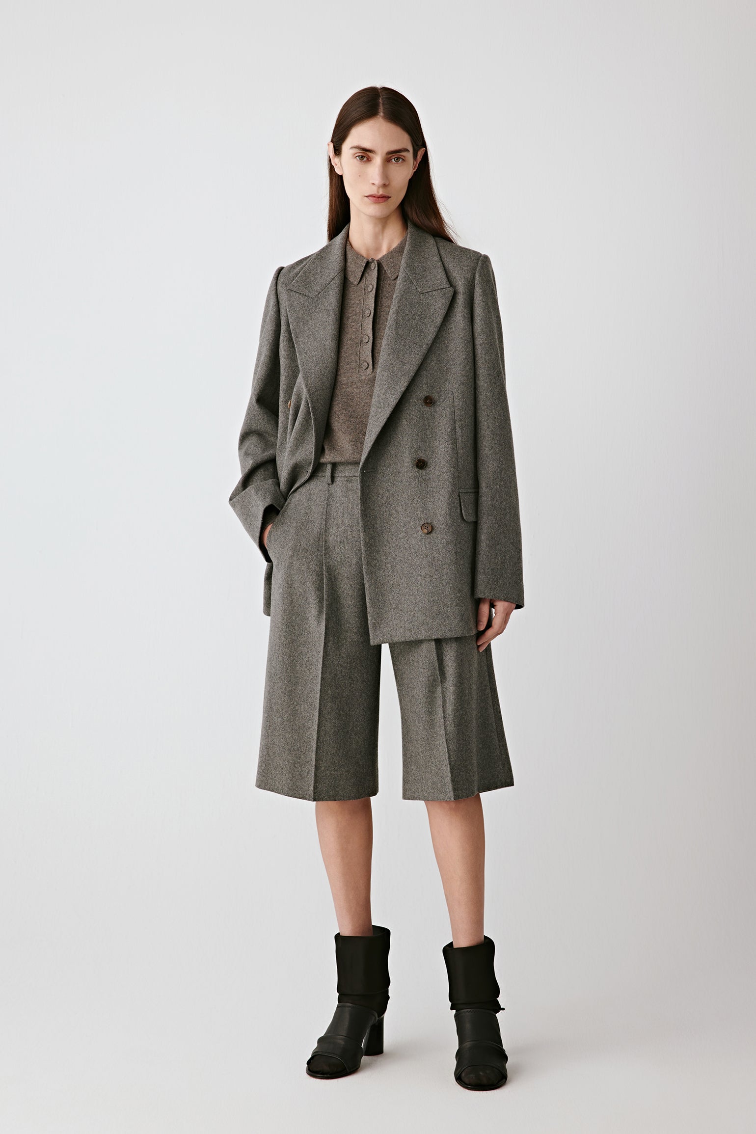 Full-length front view of the model wearing the grey melange Bermuda shorts with matching blazer.