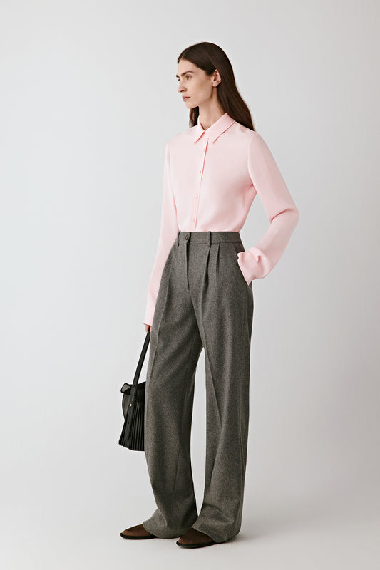 Full-length front view of the model wearing the pale pink silk crêpe shirt tucked into wide grey trousers, showing the shirt’s fluid drape and subtle sheen under soft light.