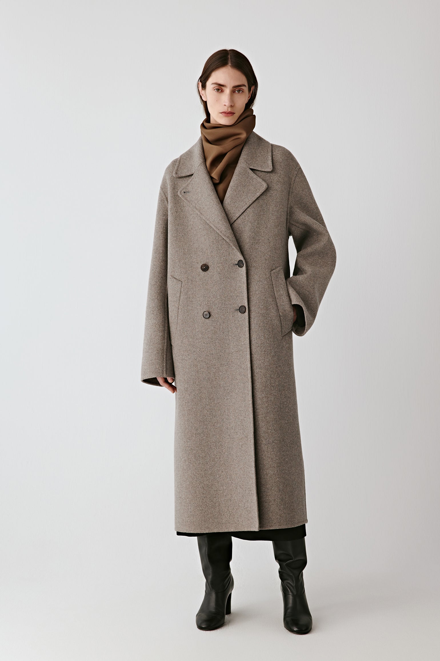 Front view of the grey melange double-breasted wool coat, styled with black boots and showing its straight cut.