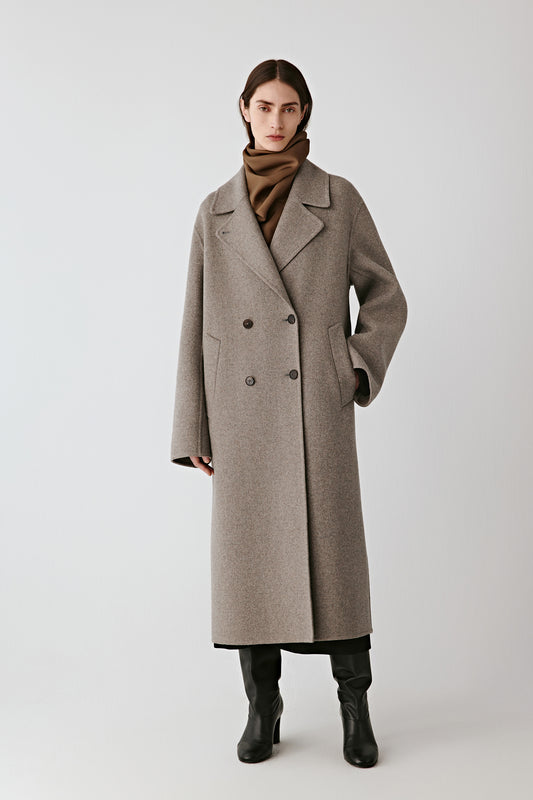 Front view of the grey melange double-breasted wool coat, styled with black boots and showing its straight cut.