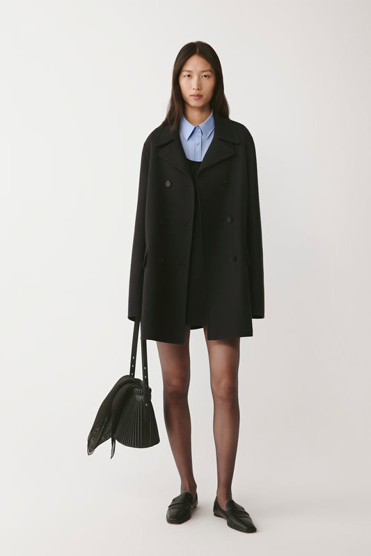 Front view of the black double-faced wool peacoat, worn over a blue shirt, with notched lapels and double-breasted fastening.