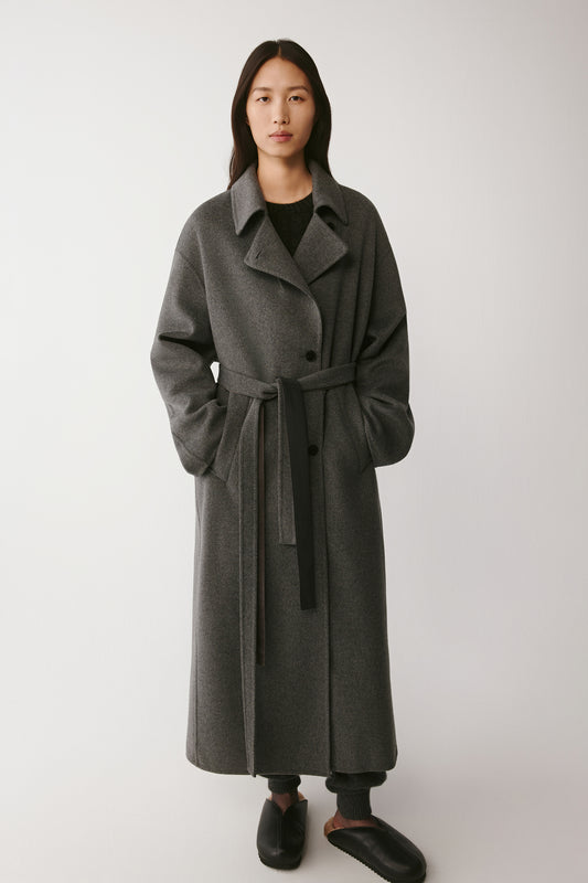 Full-length front view of the grey melange double-faced wool and silk coat tied at the waist with a matching belt.