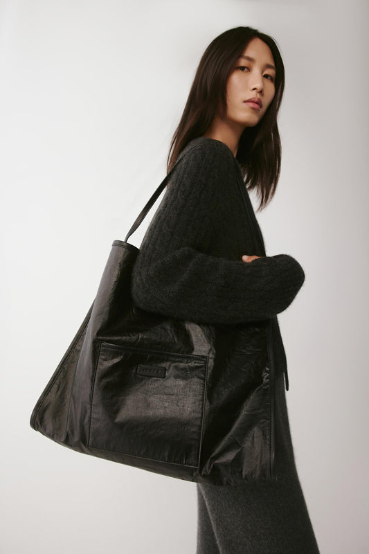Female model carrying a large black cotton tote bag over the shoulder, showing its soft, slouchy structure and wide strap.