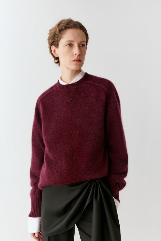 Front view of a woman wearing a burgundy cashmere pullover, highlighting the relaxed silhouette, crew neckline and ribbed trims.
