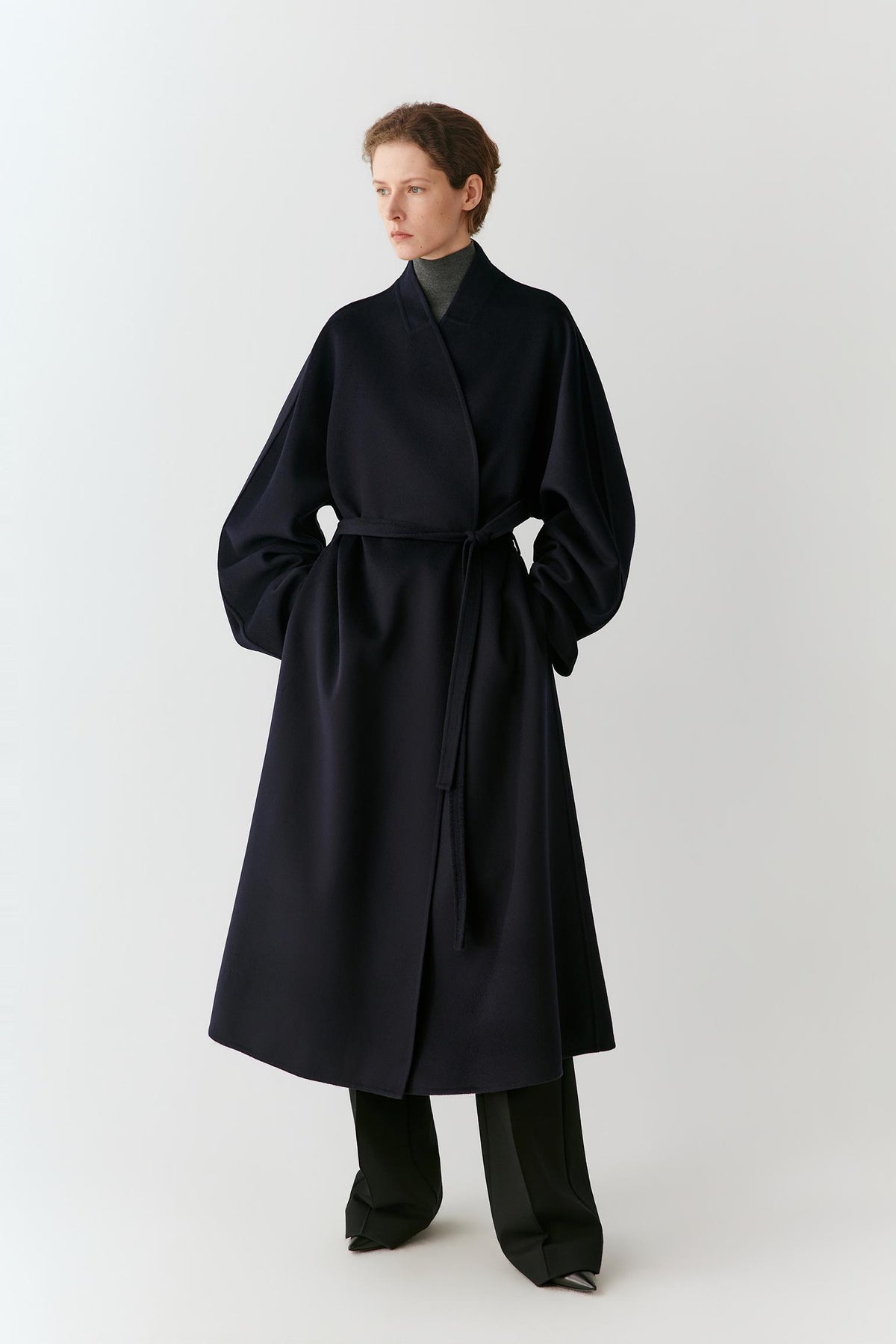 Front view of a woman wearing a navy wool coat, highlighting the long silhouette, shawl collar and self-tie belt.