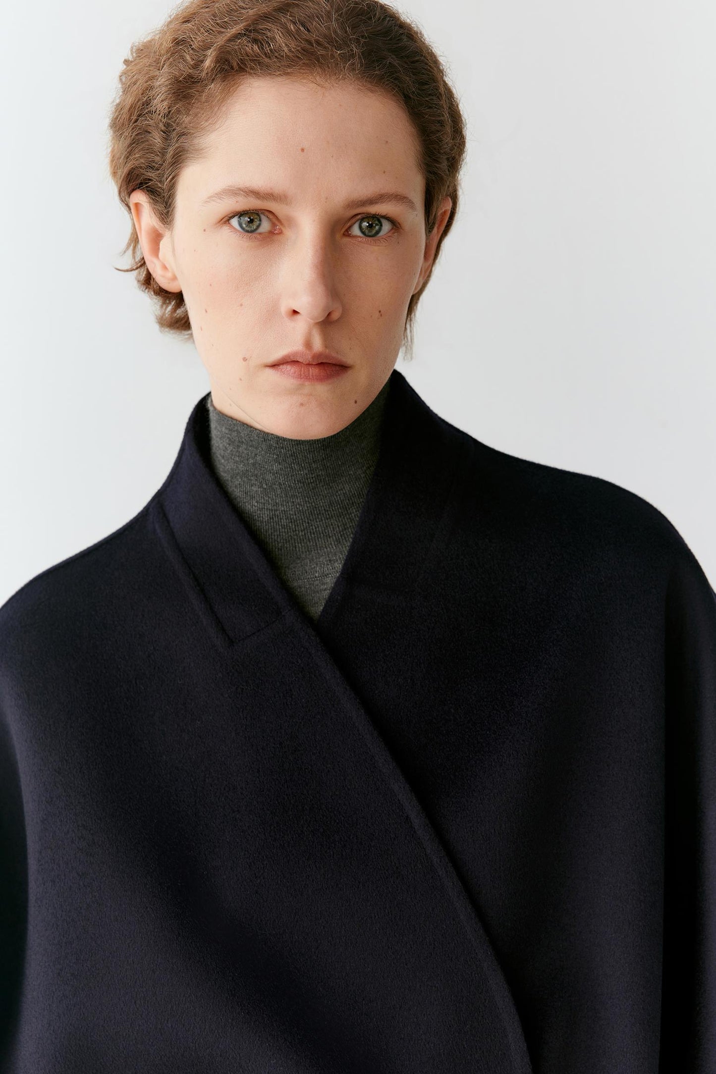 Close-up highlighting the open front, shawl collar and smooth surface of the navy wool fabric.