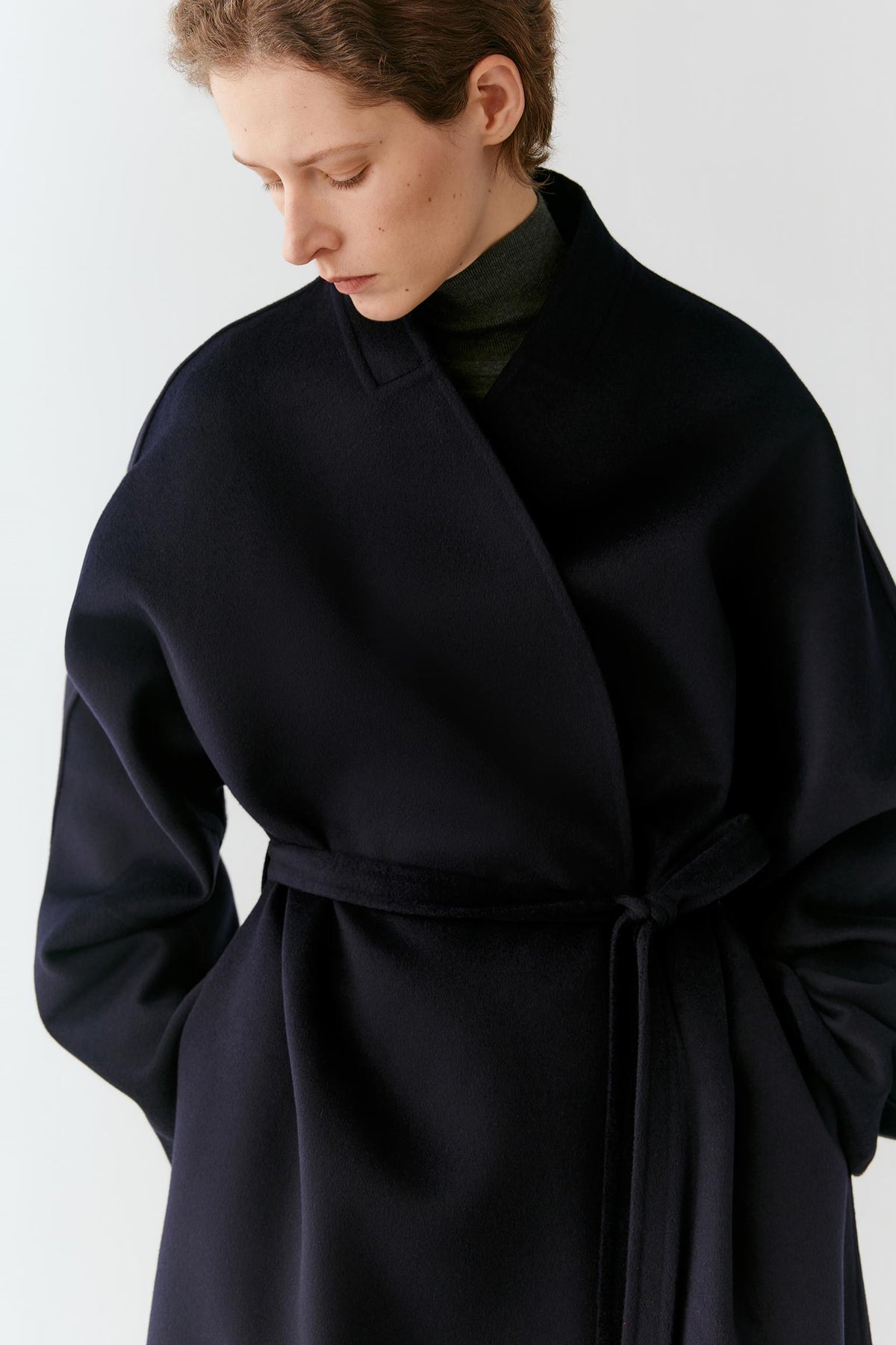 Close-up of the self-tie belt and side pocket, showing the clean construction and fluid drape of the coat.
