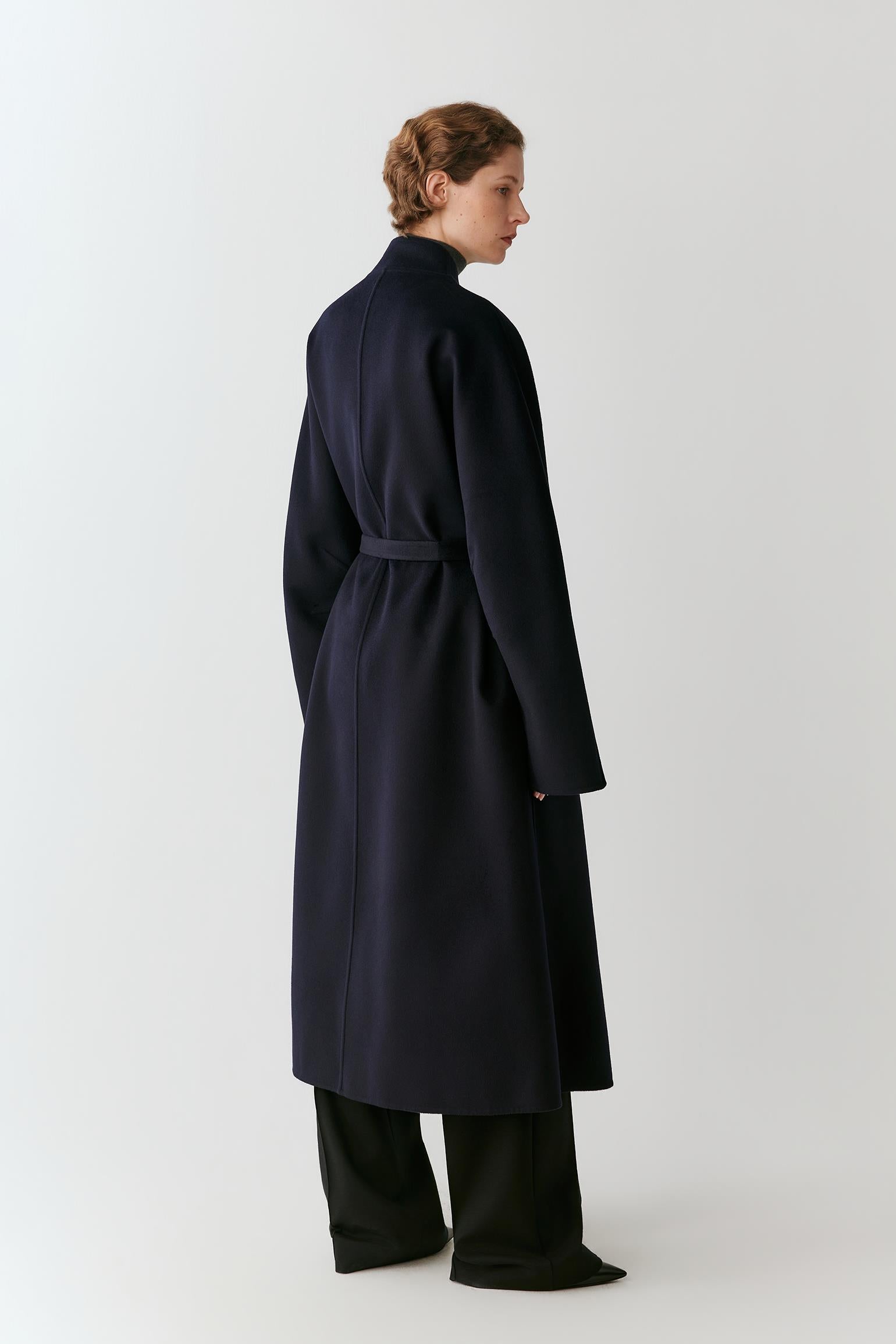 Full-length side view showing the elongated silhouette, voluminous sleeves and fluid drape of the navy fabric.