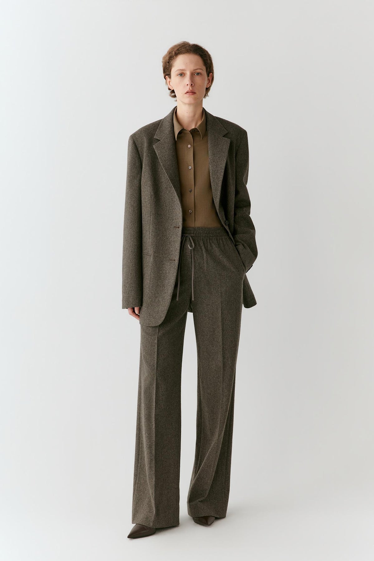 Full-length view highlighting the relaxed cut, straight lines and flap pockets of the grey melange tweed wool blazer.