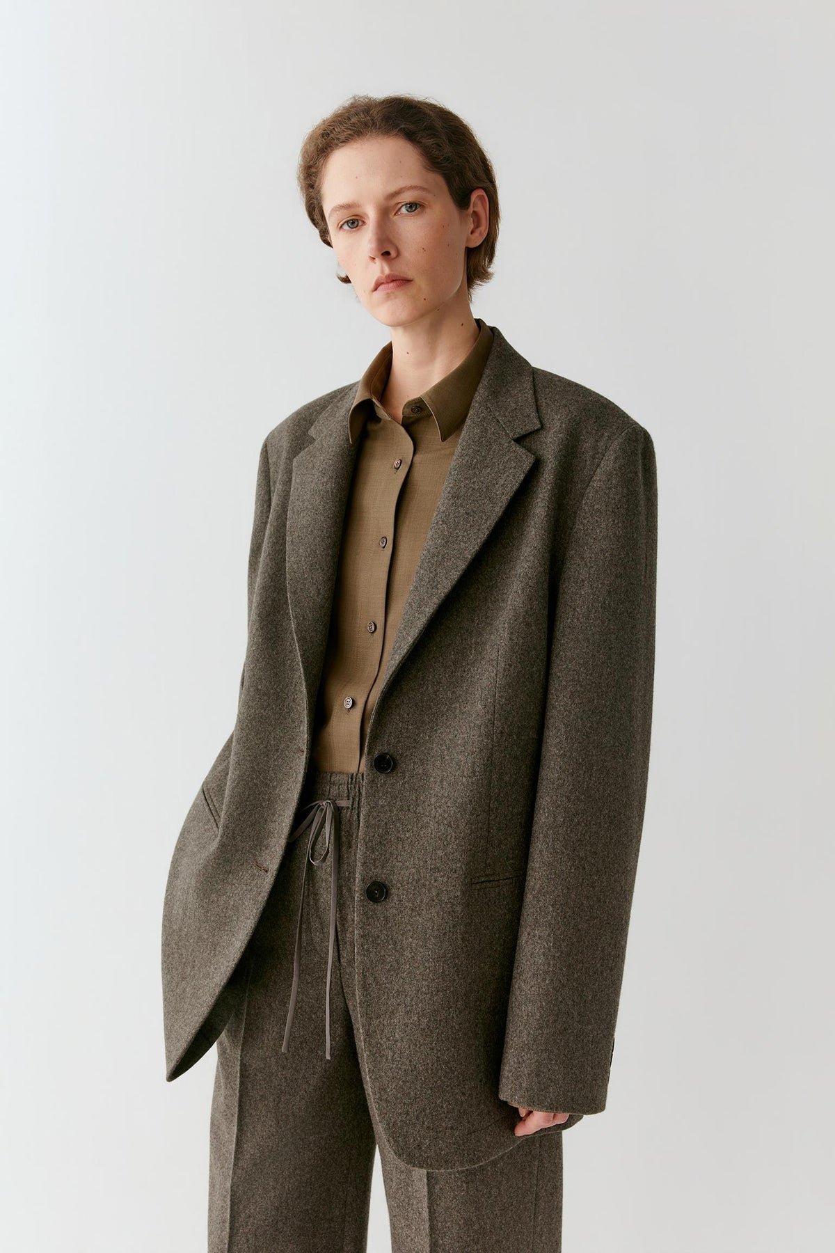 Front view of a woman wearing a grey melange tweed wool blazer, showing the relaxed single-breasted silhouette and notched lapels.