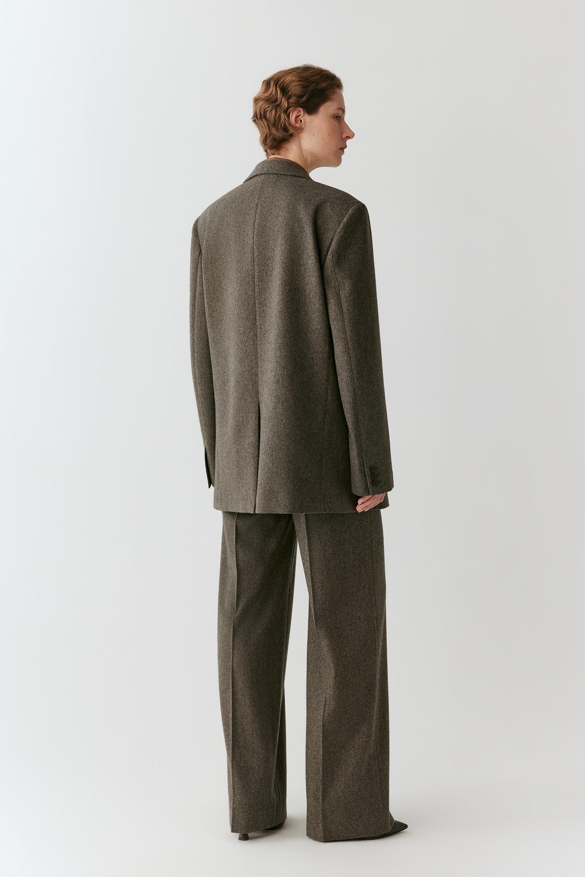 Back view showing the relaxed silhouette and structured woven texture of the grey melange tweed wool blazer.