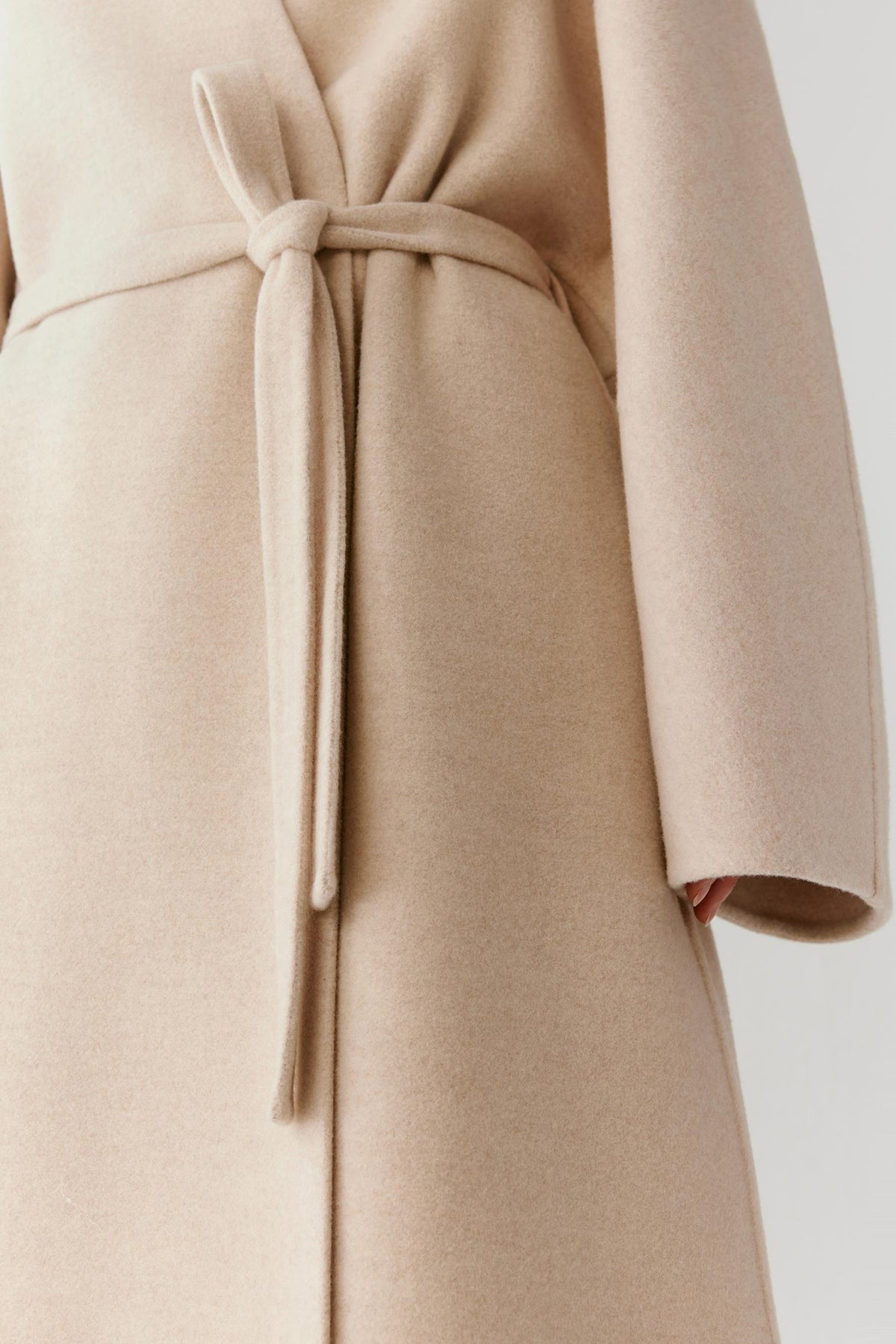 Close-up highlighting the self-tie belt and clean-cut edges of the beige melange coat.