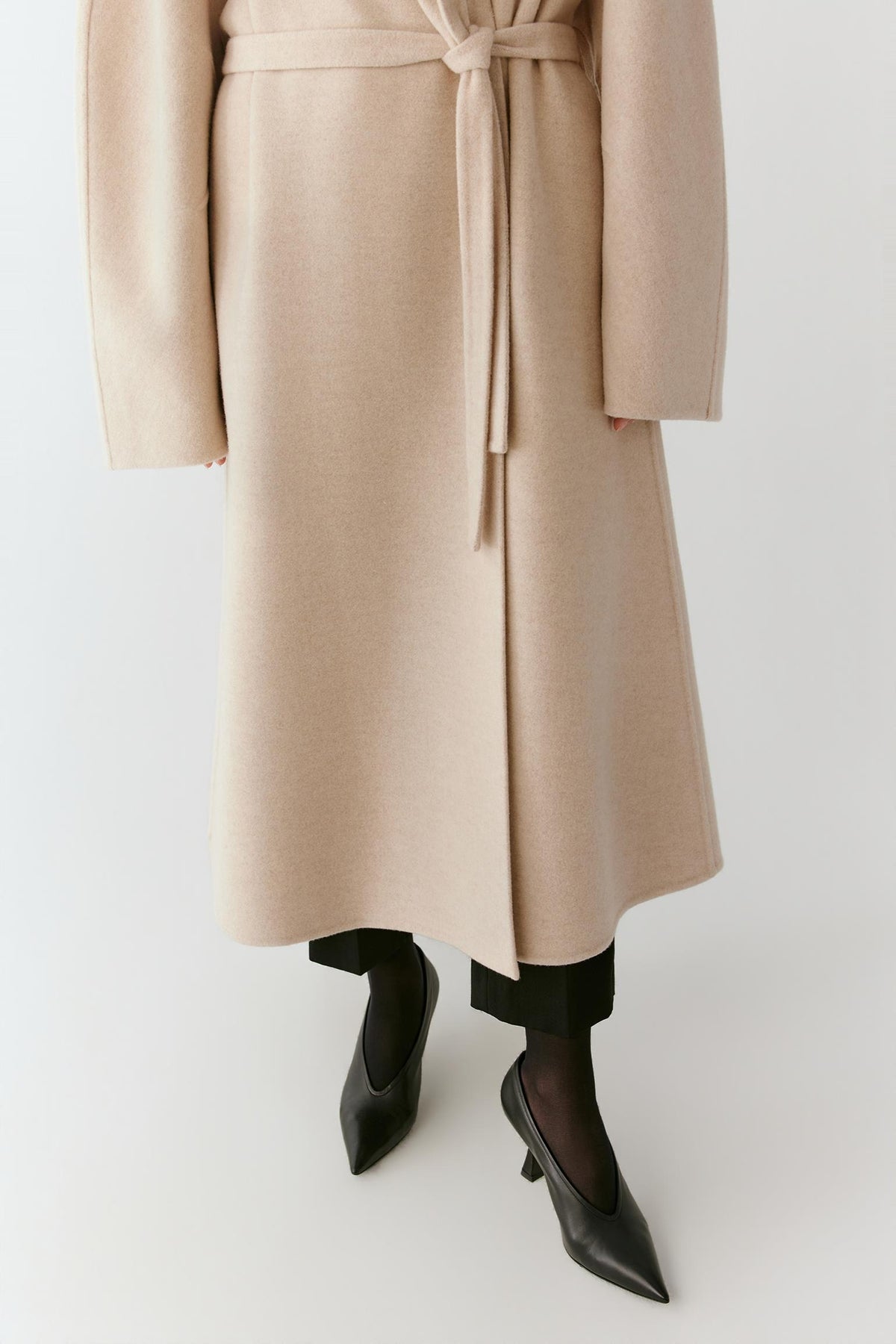 Full-length view highlighting the long hem, wrap construction and fluid drape of the beige melange wool and cashmere coat.