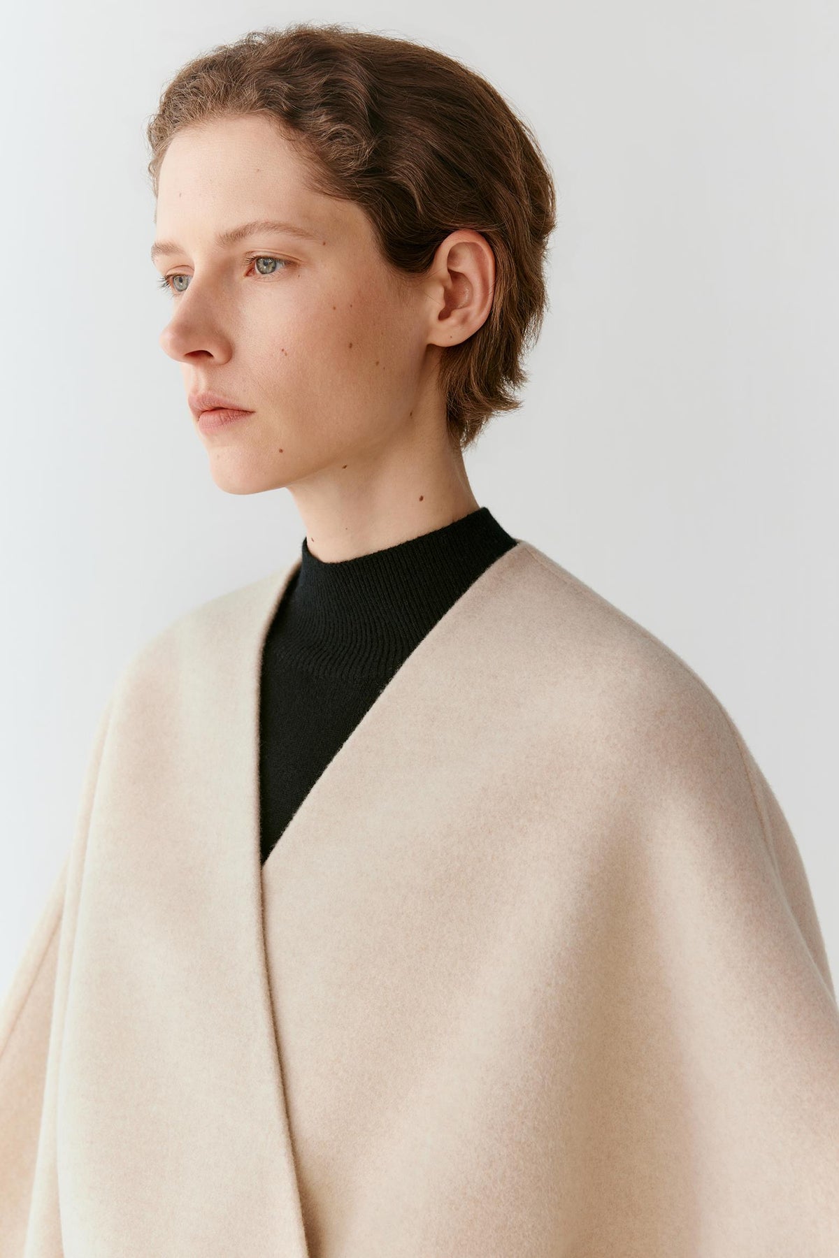 Close-up highlighting the V-neckline, wrap front and smooth beige melange wool and cashmere surface.