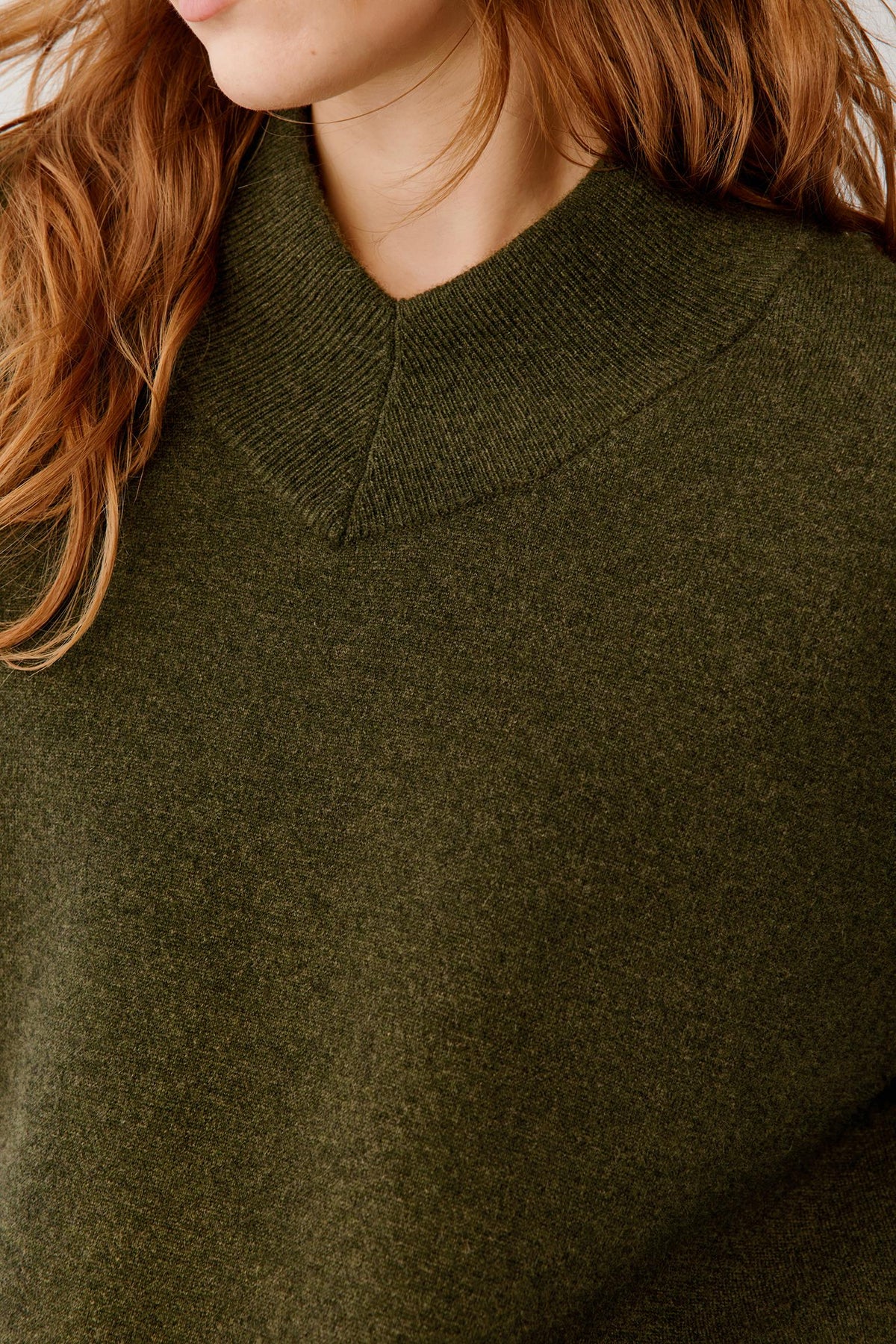 Close-up of a person wearing a soft knit sweater in an olive green color, showing the ribbed v-neck collar and textured fabric.
