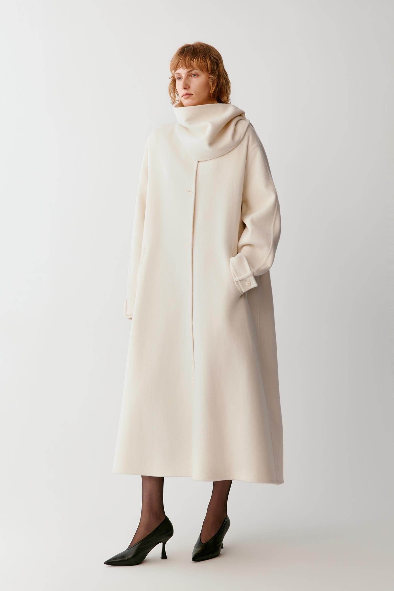 Front view of a woman wearing an ivory wool and cashmere coat, highlighting the long silhouette, folded stand collar and clean construction.