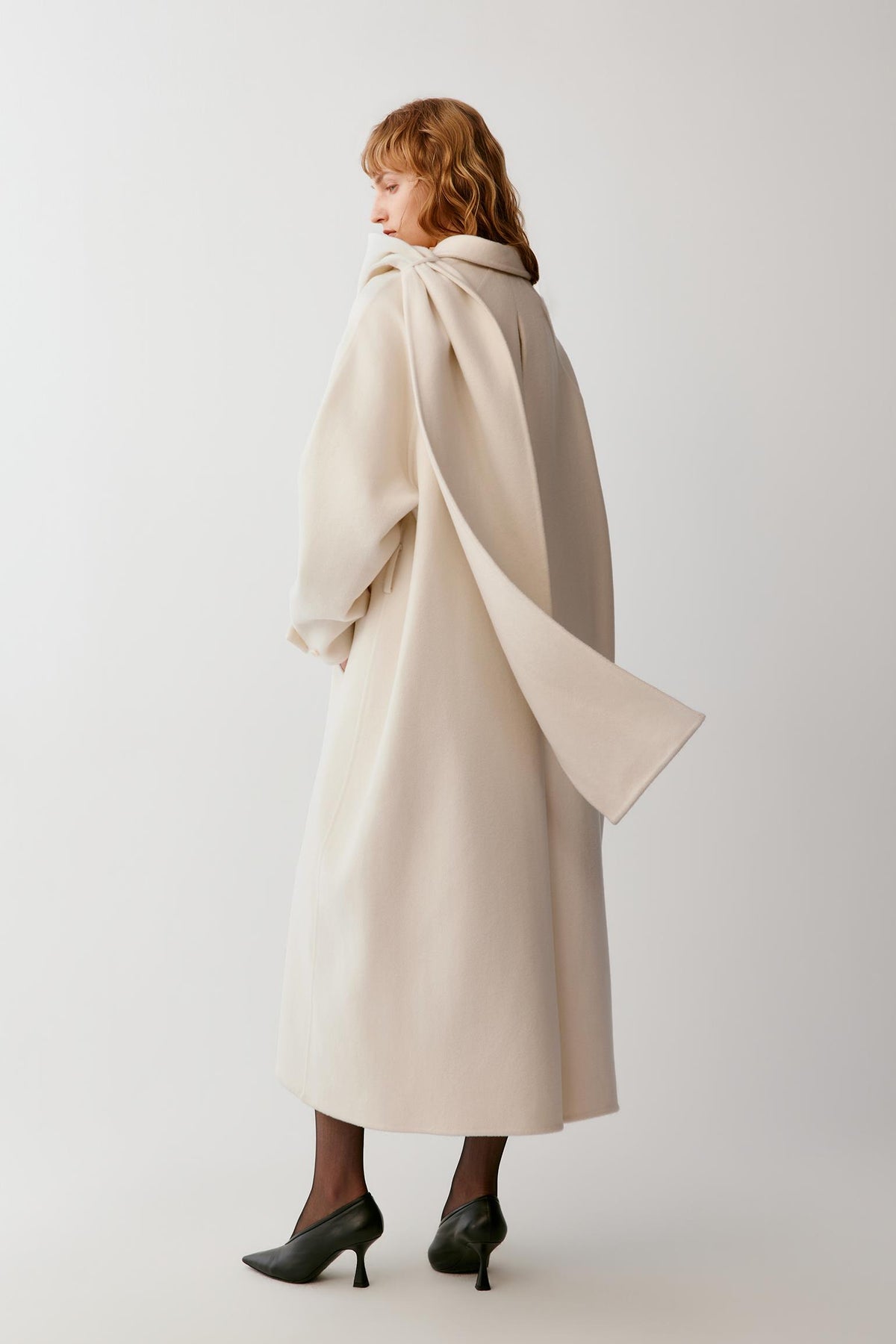 Side view highlighting the long silhouette, slanted pocket and clean lines of the ivory coat.
