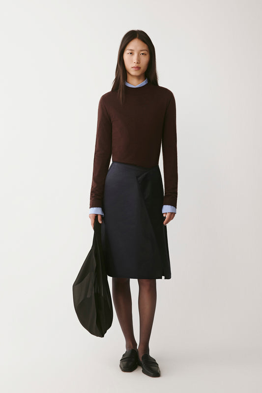 Front view of the coffee-brown cashmere mock-neck pullover, styled with a navy skirt and black bag.