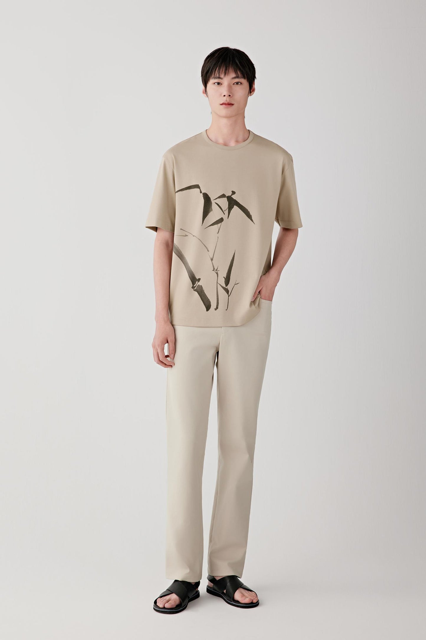 Man wearing nude straight-leg trousers with a beige top, full-length front view.