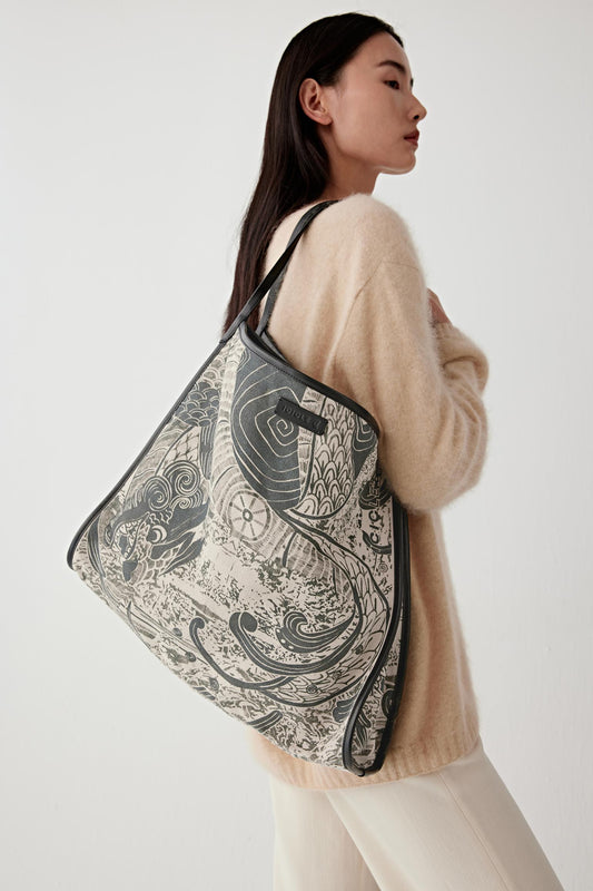 Woman carrying a large tote bag with a black and white pattern on a plain background