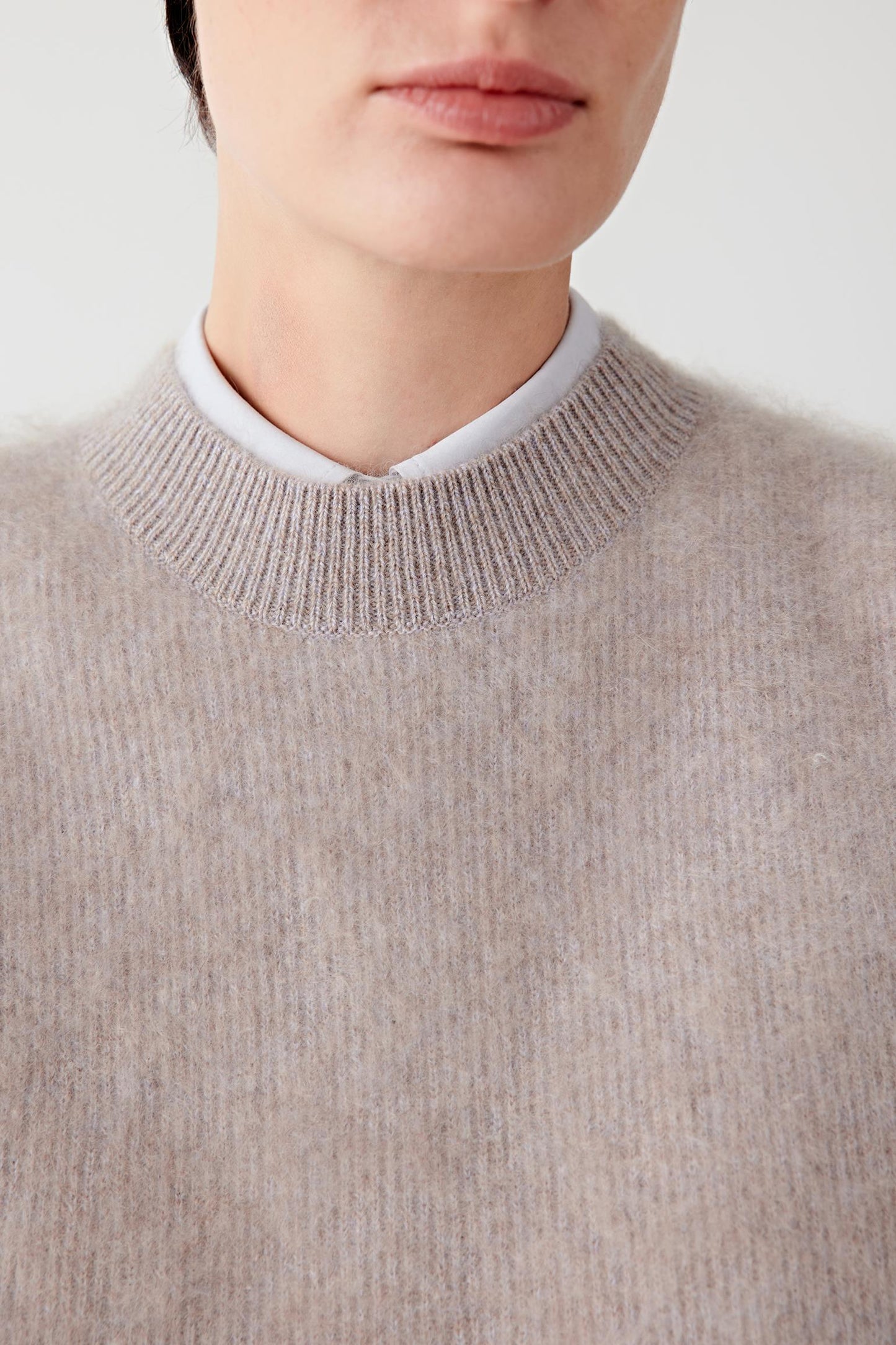 Close-up of the neckline and upper chest, revealing the fine knit structure and mélange effect.