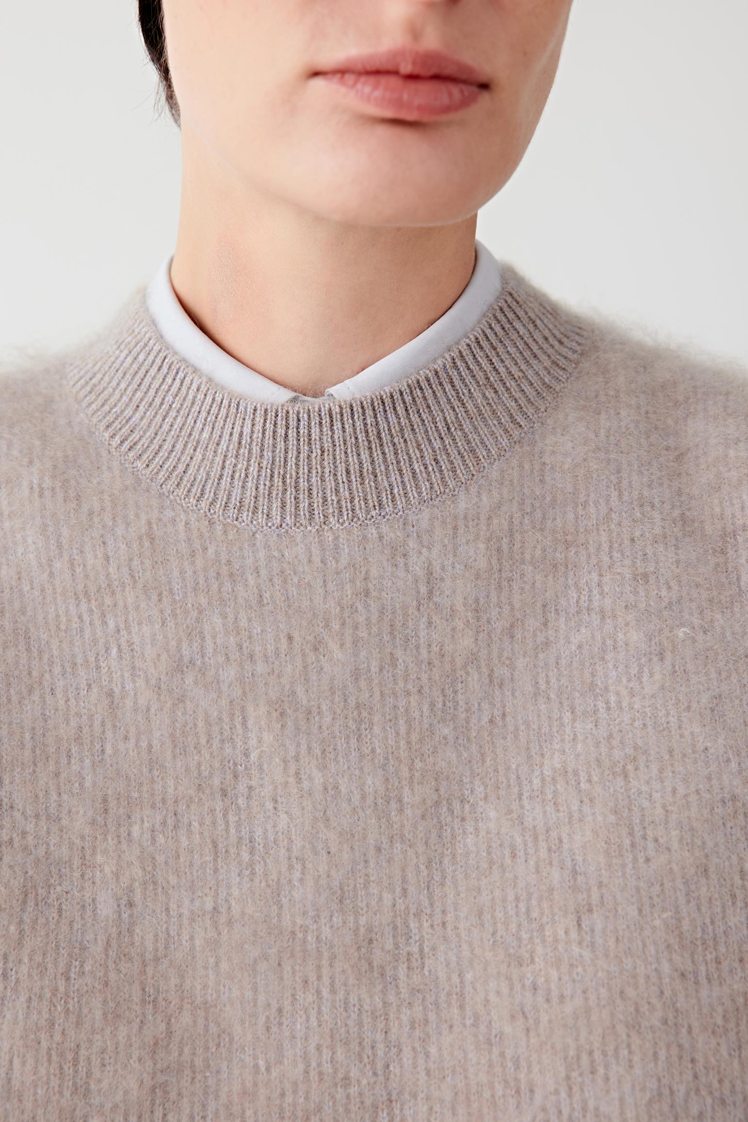 Close-up of the neckline and upper chest, revealing the fine knit structure and mélange effect.