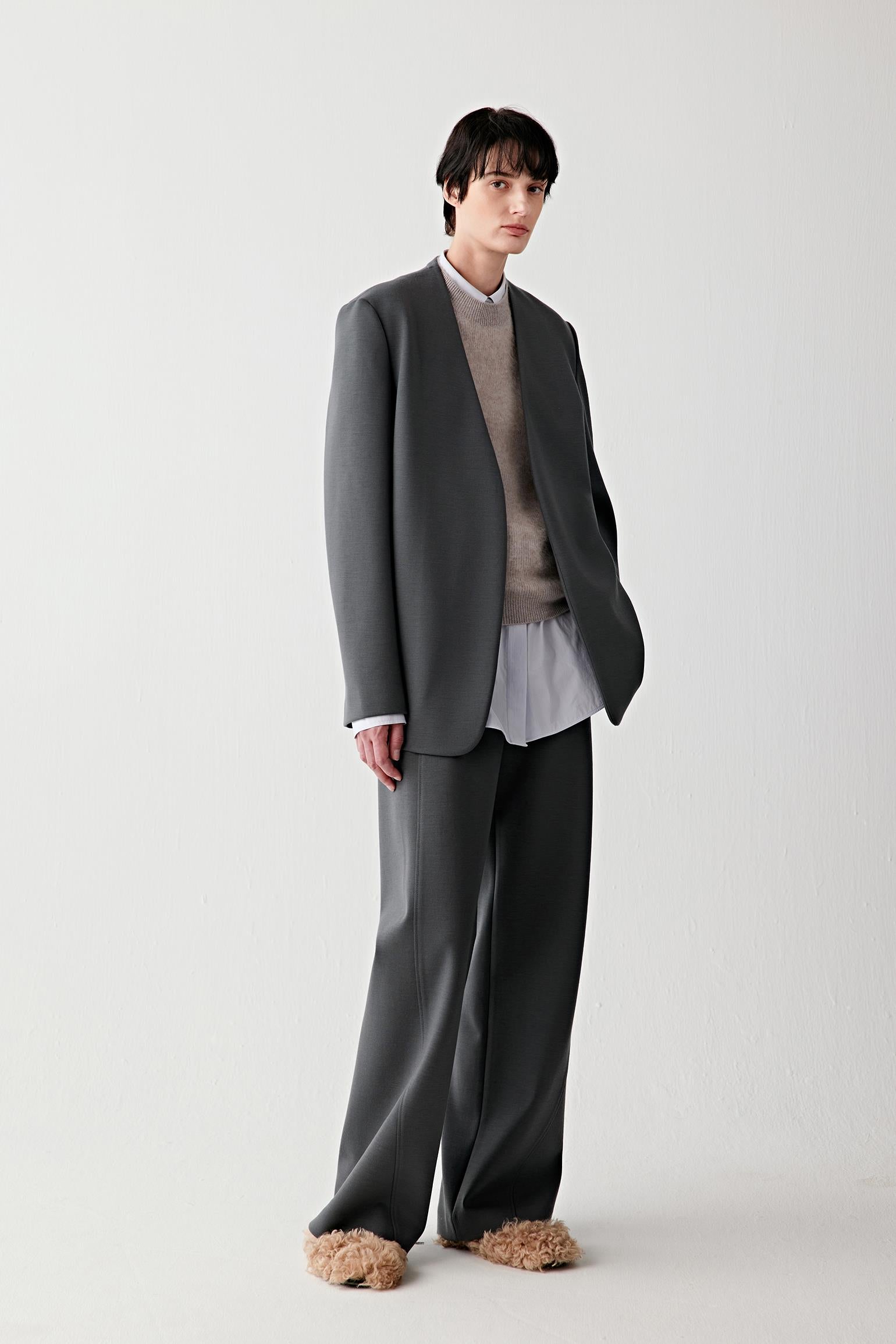 Full-length front view of a structured wool jersey jacket in deep charcoal grey, styled with wide-leg trousers.