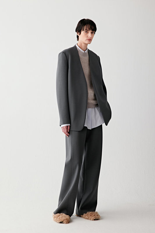 Full-length front view of a structured wool jersey jacket in deep charcoal grey, styled with wide-leg trousers.