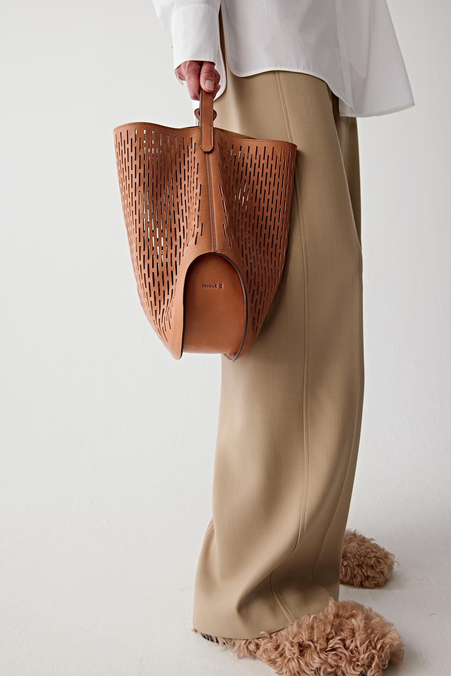 Detail view of the bag held by hand, highlighting the perforated leather texture and soft construction.
