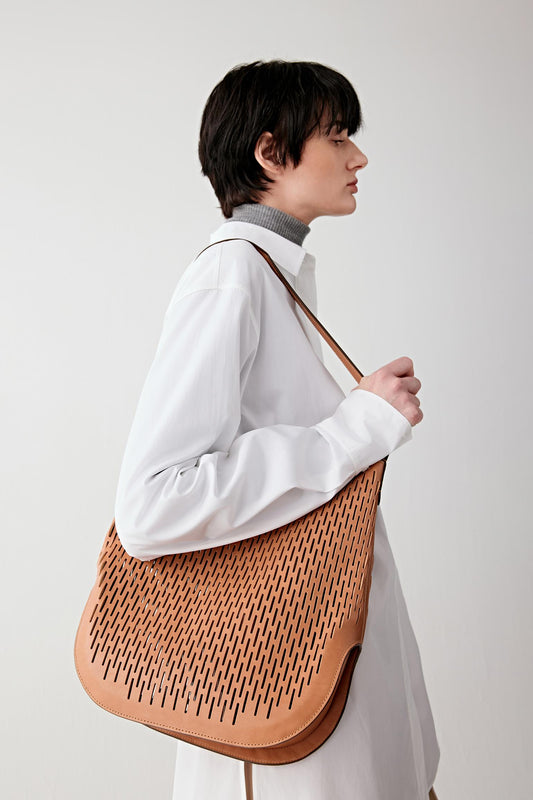 Woman wearing a camel perforated leather hobo bag with a soft slouchy silhouette, carried over the shoulder, side view highlighting the supple drape and curved shape.