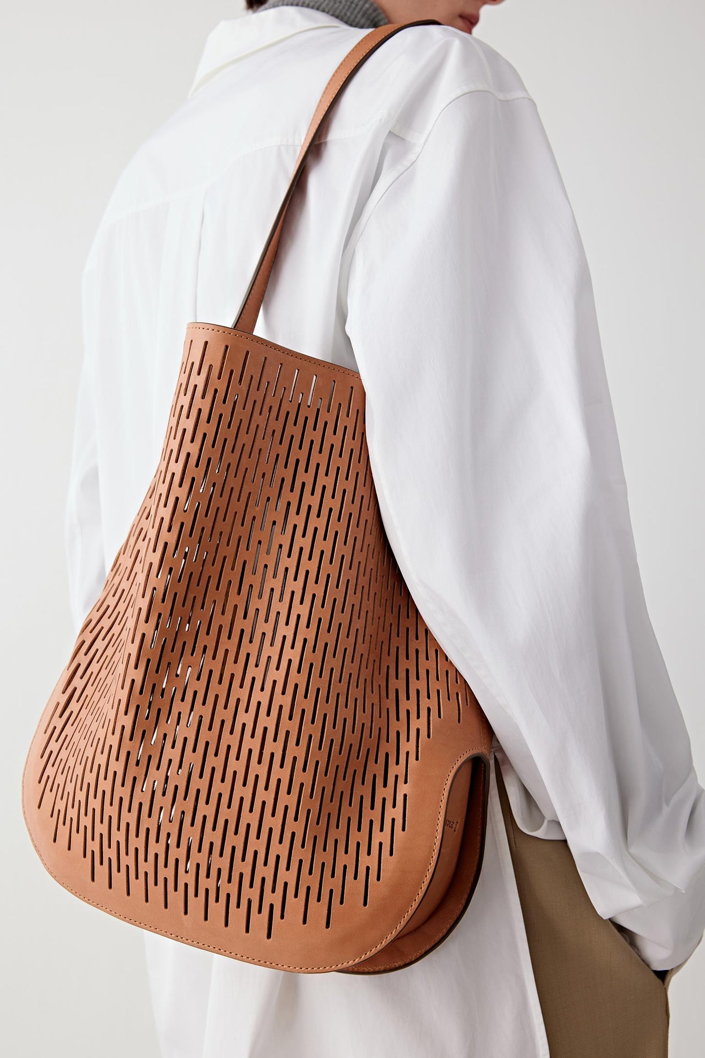 Close-up of the tan perforated leather surface and shoulder strap, emphasizing the graphic pattern, texture and flexibility of the material.