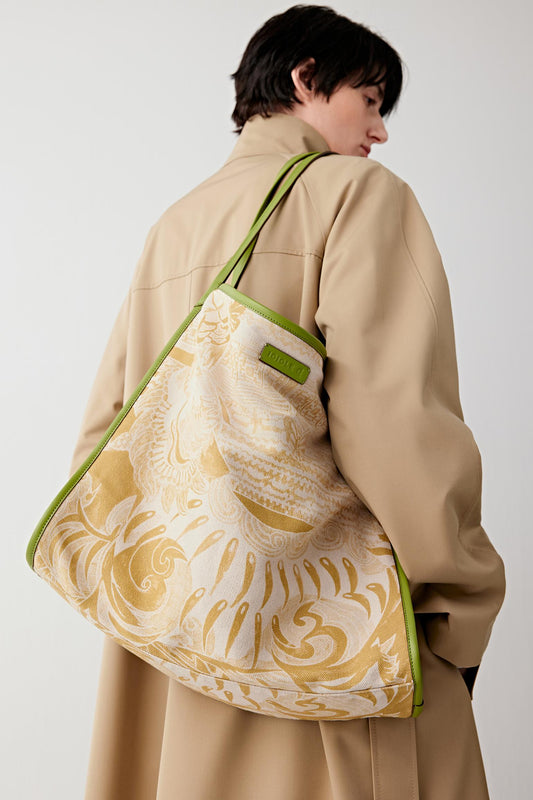 Woman wearing a large tote bag in linen and cotton with a beige base and yellow White Tiger motif, carried on the shoulder, back three-quarter view highlighting the soft structure and wide strap.