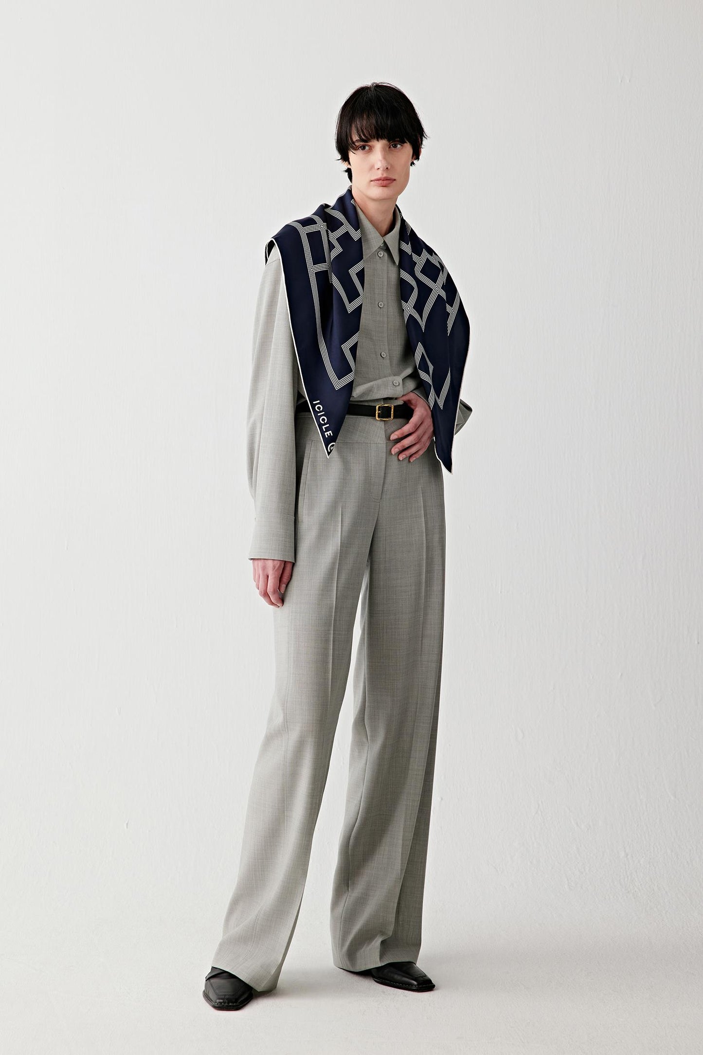 Full-length view of the model standing, wearing the silk twill scarf loosely around the neck, highlighting how the scarf integrates into the outfit, its medium weight, clean fall and graphic pattern distribution across the fabric