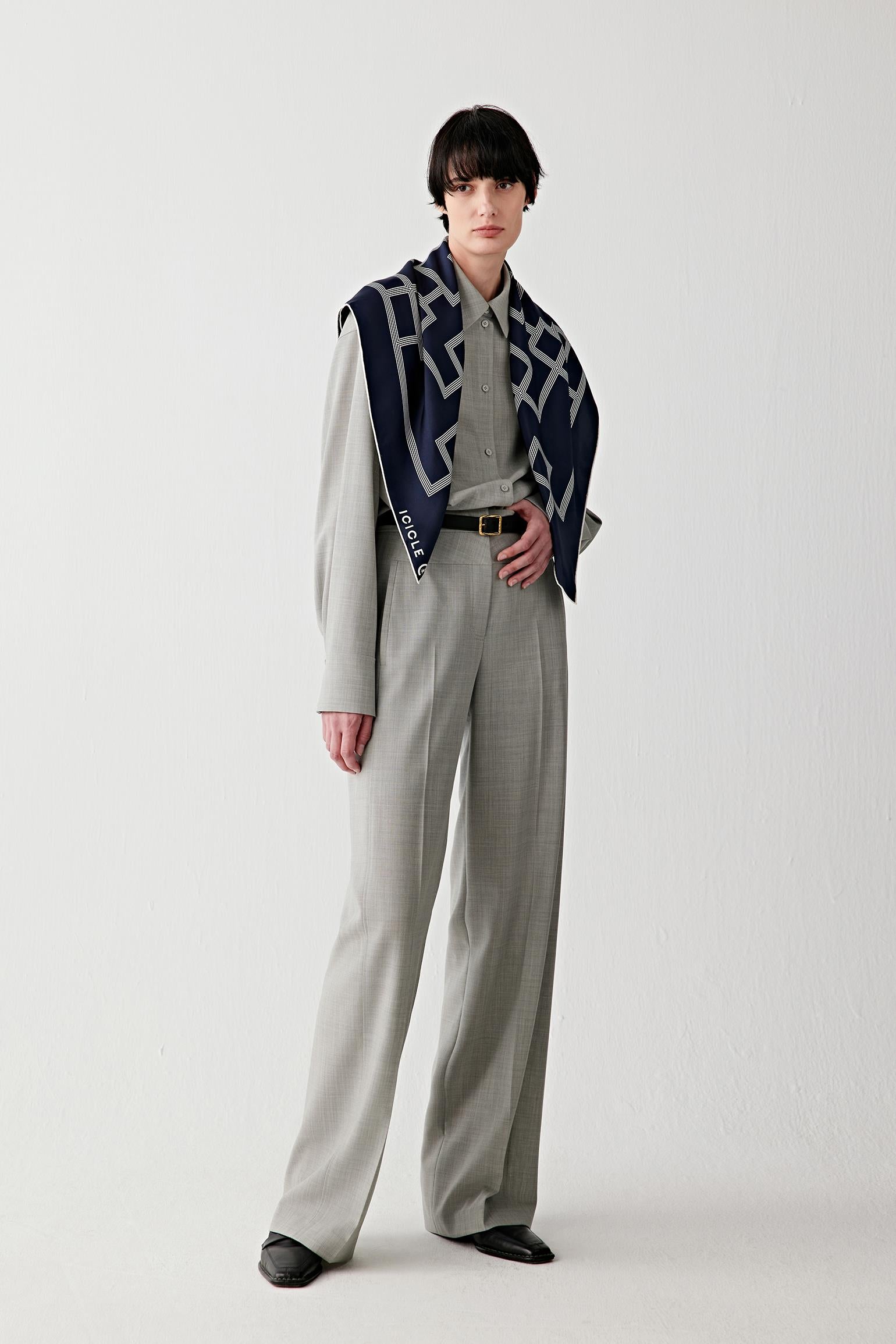 Full-length view of the model standing, wearing the silk twill scarf loosely around the neck, highlighting how the scarf integrates into the outfit, its medium weight, clean fall and graphic pattern distribution across the fabric