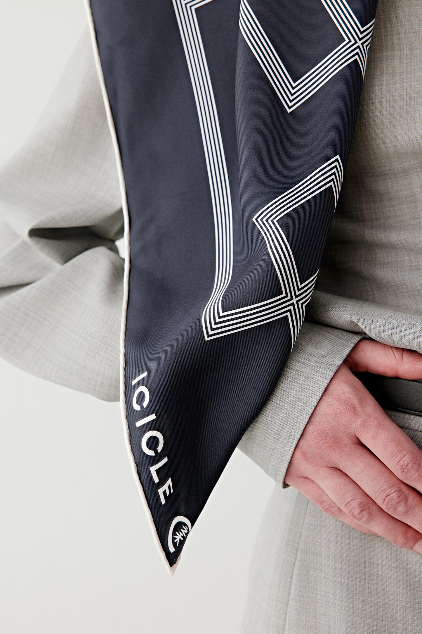 Close-up of the scarf corner held in hand, showing the fine silk twill texture, precise printed pattern, hand-rolled or clean finished edges and slight sheen of the fabric