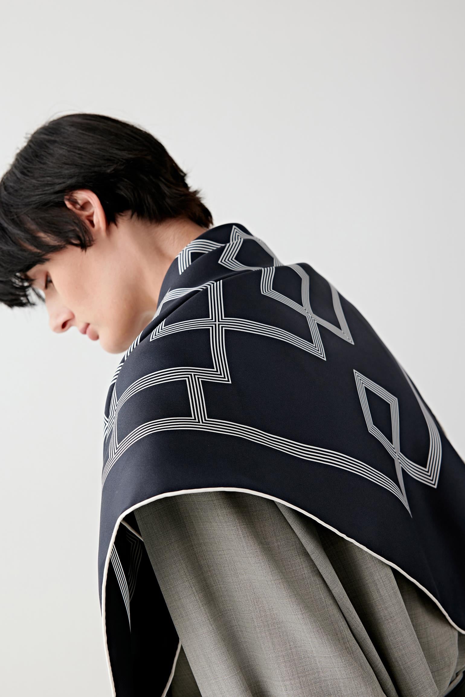 Back three-quarter view focusing on how the scarf sits across the shoulders, showing the continuity of the geometric motif, the flat drape and the way the fabric holds its shape