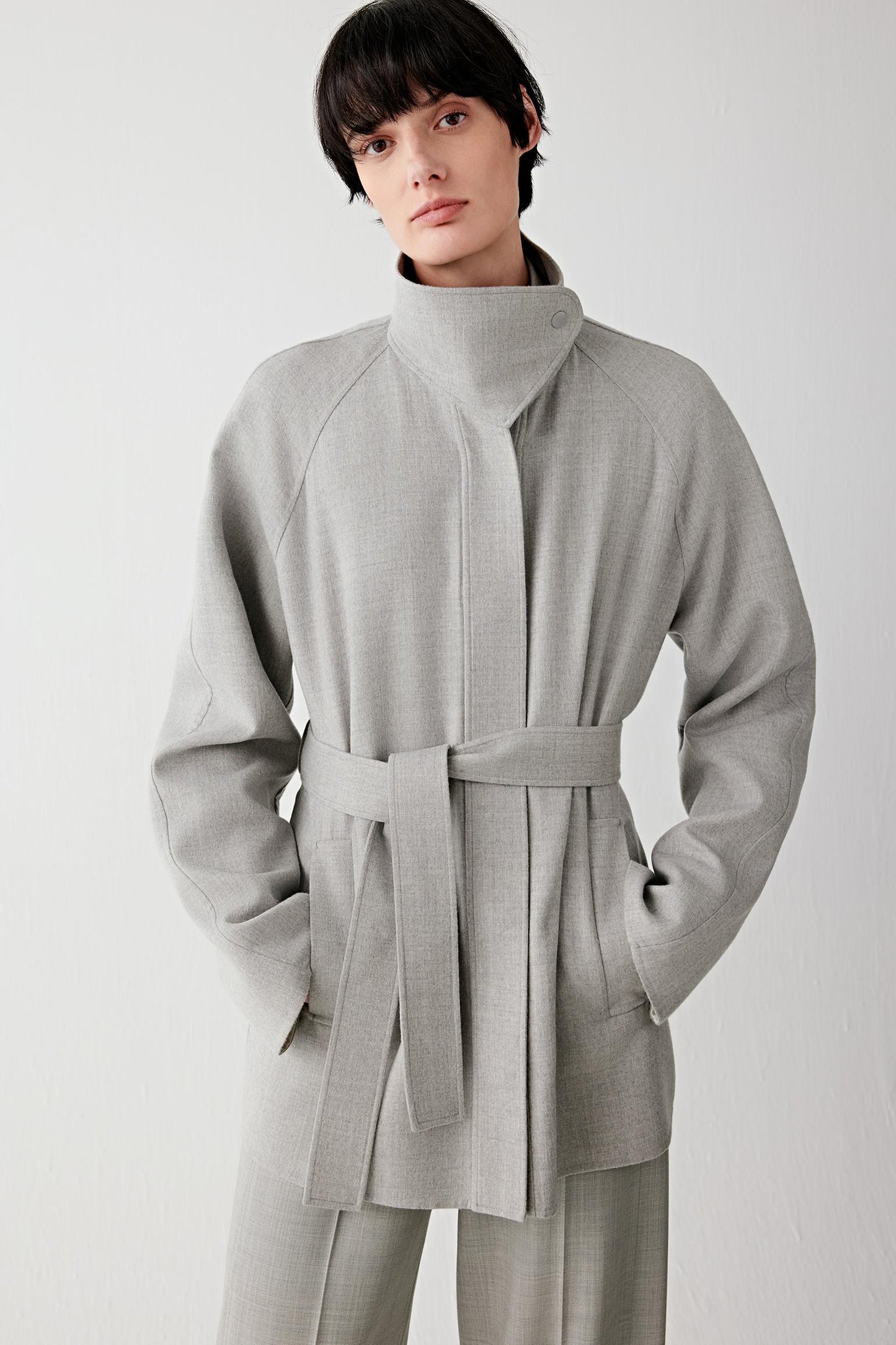 Front three-quarter view highlighting the wrap-style front, adjustable belt and slightly dropped shoulders, creating a loose, comfortable fit.
